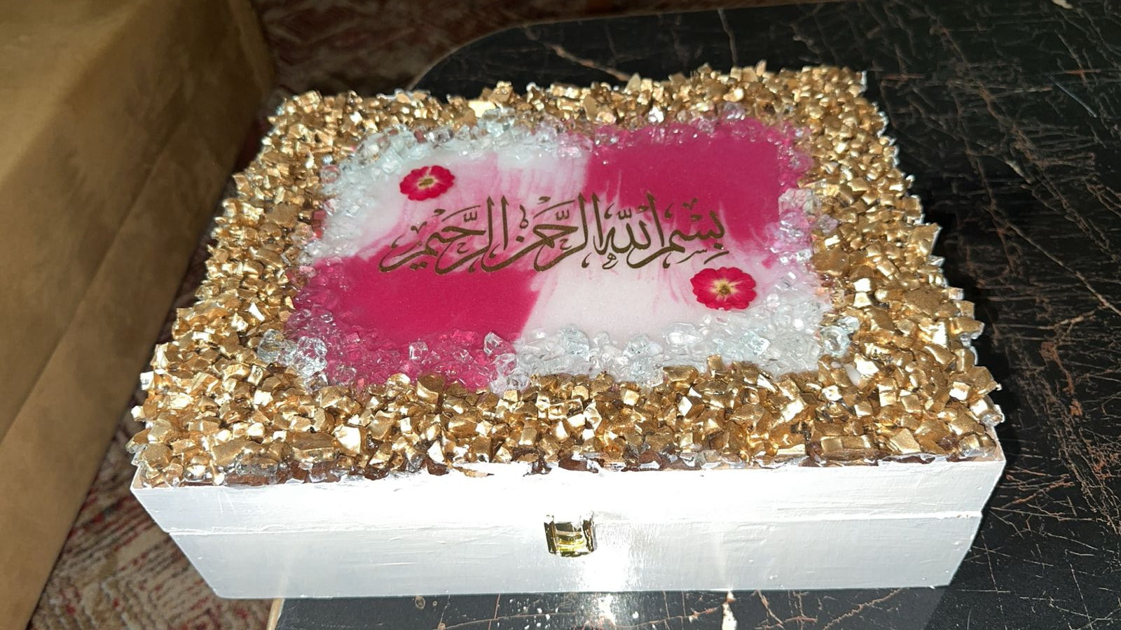 Decorative box with gold glitter border and pink interior on a textured surface